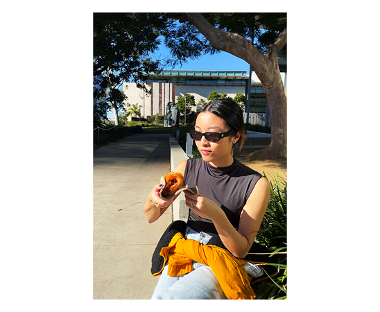Jessica Lim Account executive at Spruik, eating a donut sitting down outside in the sunshine with a tree and building behind her. Text reads "Doing the thinking for my clients."