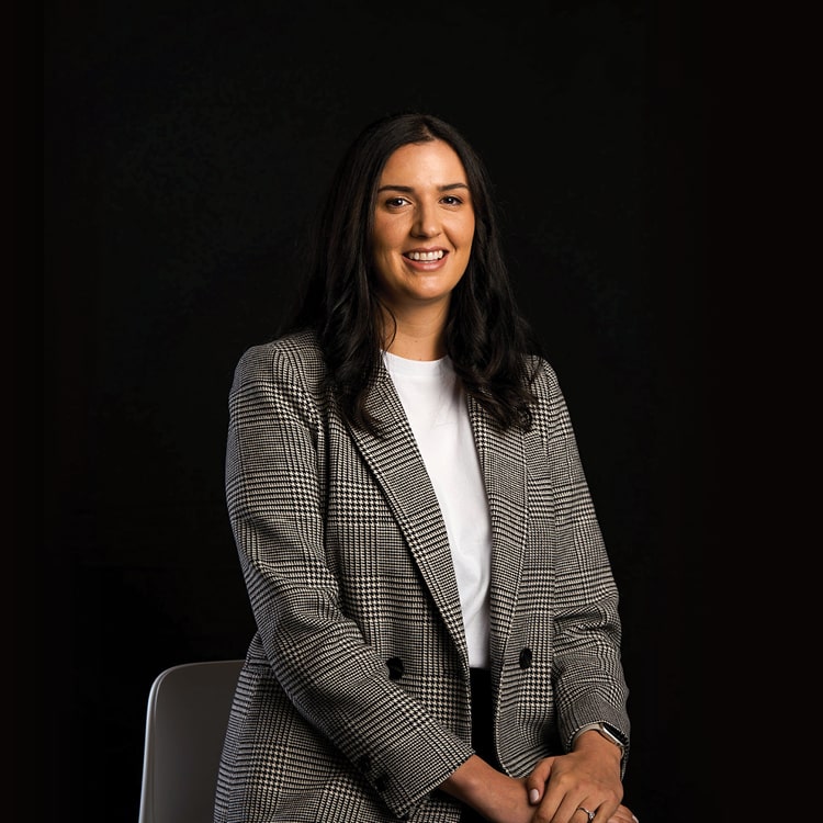 Kate White, Account Director at Spruik, wearing a blazer while smiling and looking at the camera with a black background.