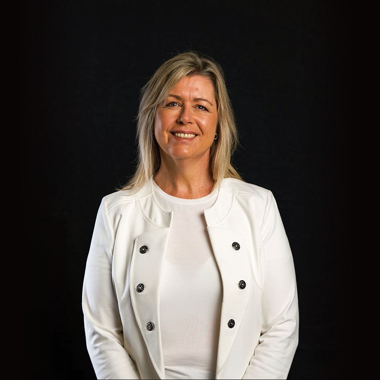 Kathryn Dunn, Business Director at Spruik wearing a white jacket while smiling, looking into the camera with a black background.