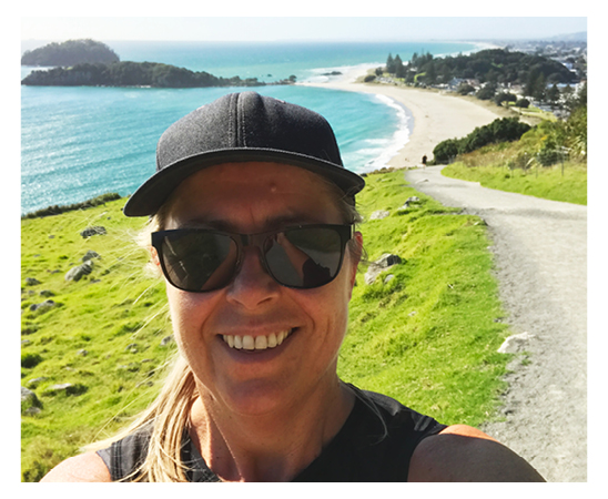 Kathryn Dunn Business Director at Spruik, smiling outside exercising in the sun, with the ocean, beach and mountain in the background.