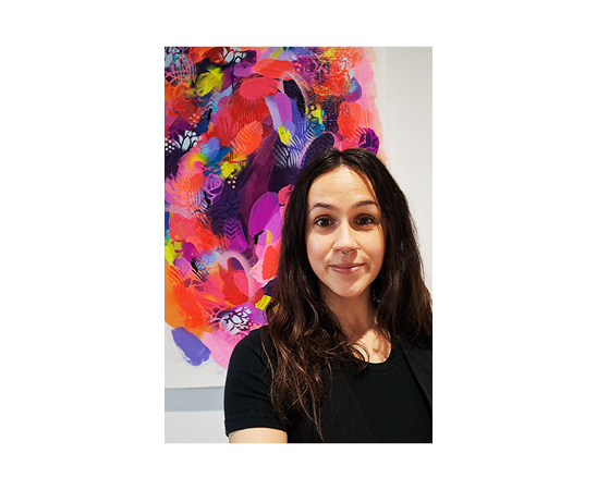 Lucie Blazevska Senior Designer at Spruik, standing in front of her colourful artwork while smiling and wearing a black top.