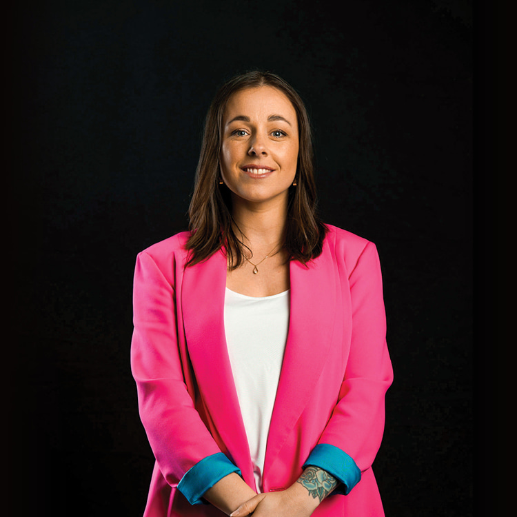 Stacey Morrisey, Creative Director at Spruik, wearing a pink jacket and smiling with a black background.